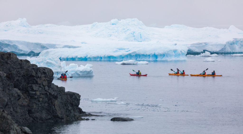 Kayakers on the water next to icebergs. 