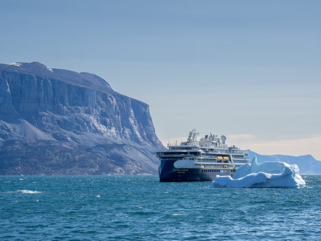 The ship National Geographic Resolution sailing next to iceberg. 