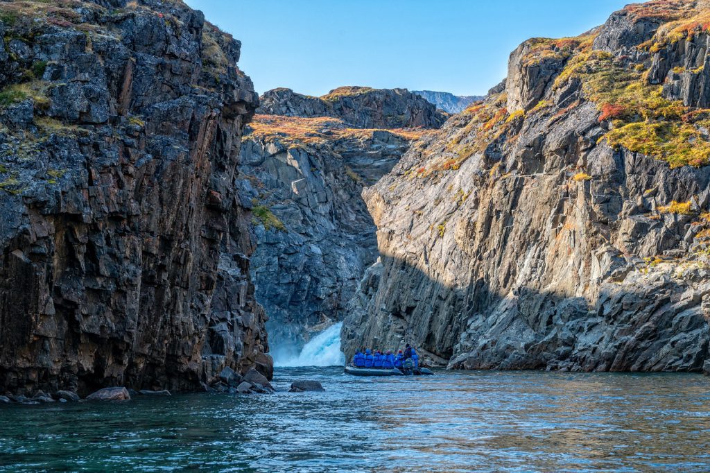 A zodiac on the water next to steep rock cliffs.