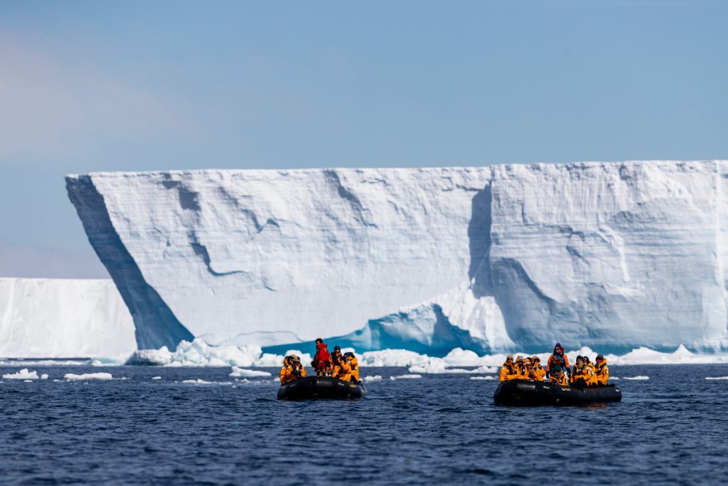 Two zodiacs on the water next to massive tabular icebergs.