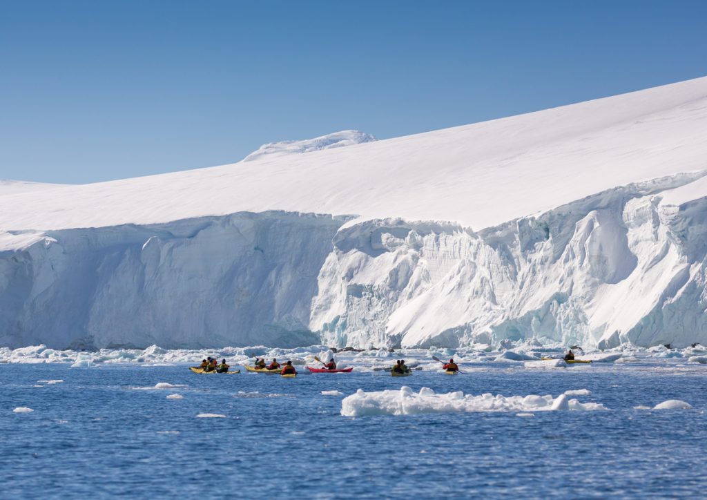 Kayakers on the water next to glacier face.