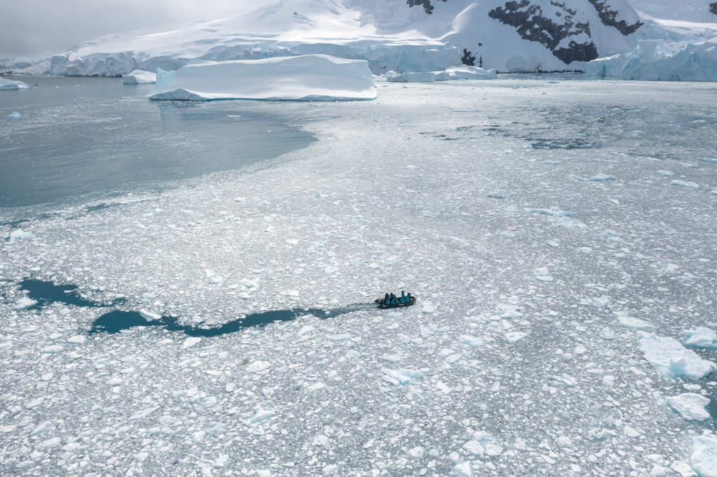 Drone shot of zodiac cruising in icy bay in Antarctica. 