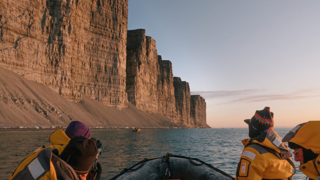 Guest in zodiac on the water looking at dramatic cliff. 