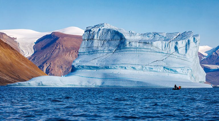 Large iceberg with zodiac on the water nearby.